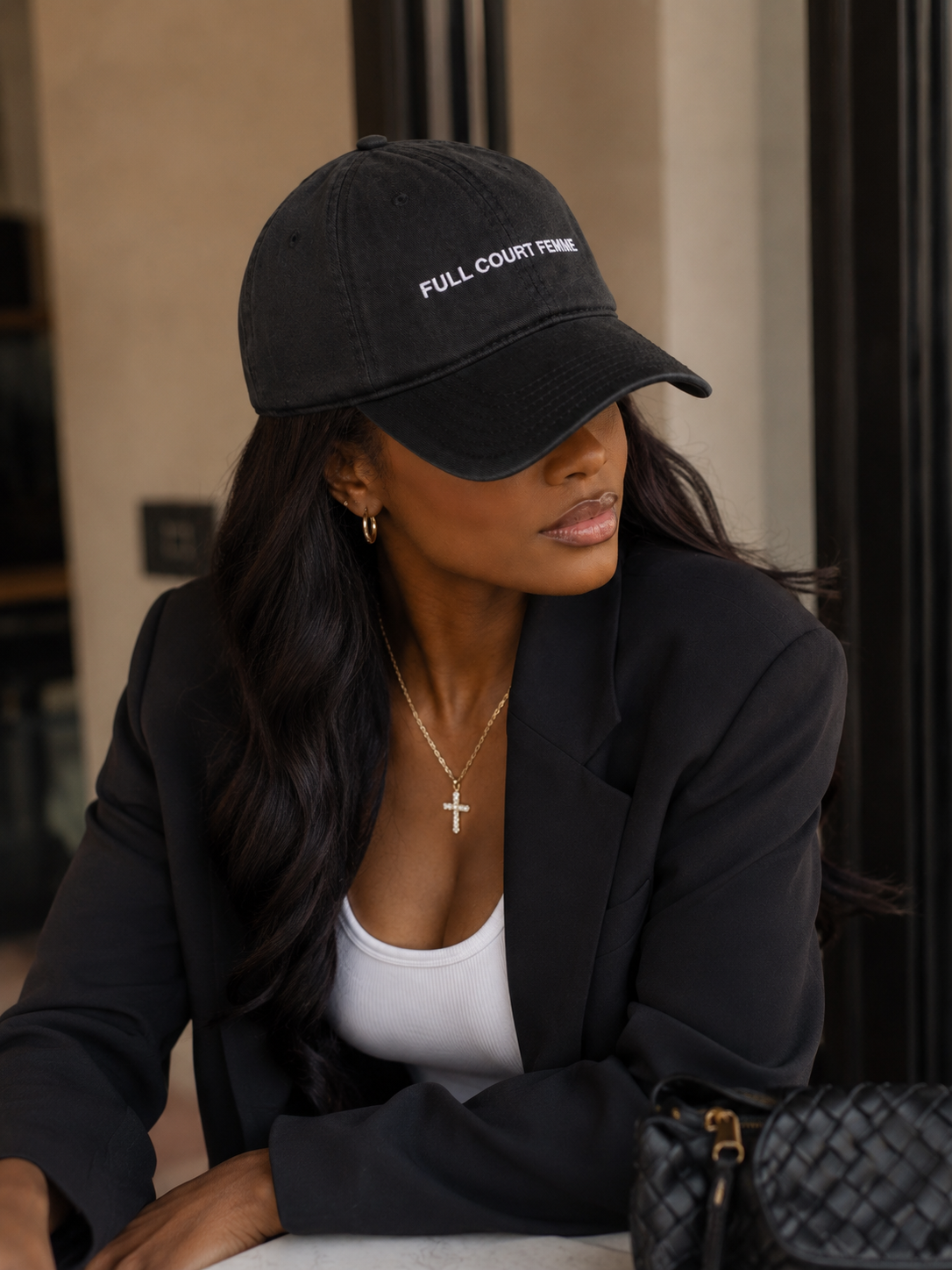 Lifestyle photo of a woman wearing the Full Court Femme embroidered black cap with a tailored black blazer and white tank top.